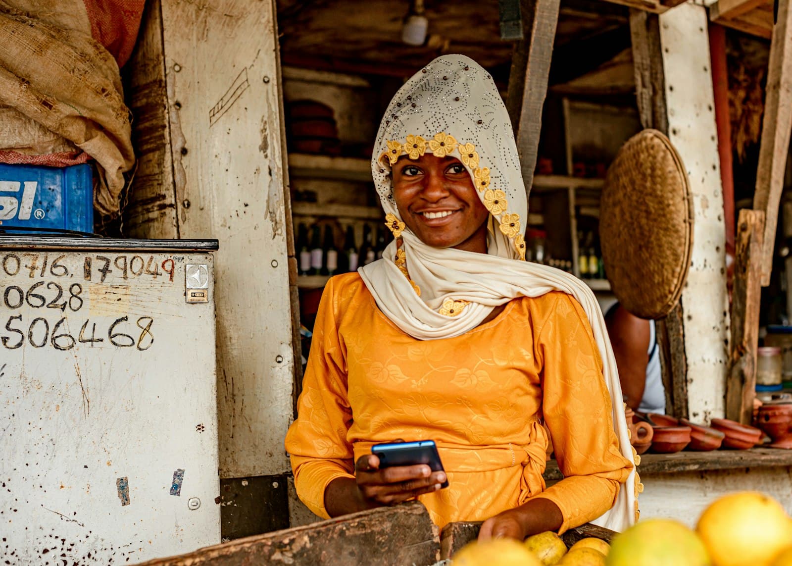 Commerçante souriante devant son étal, un téléphone à la main